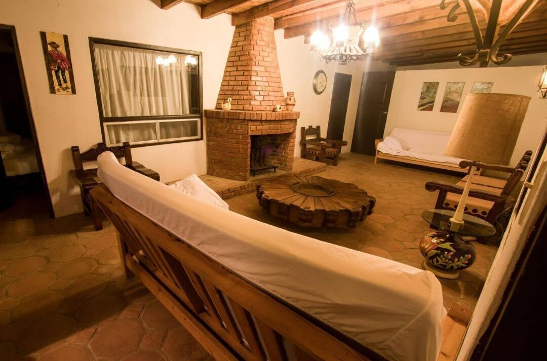 Uma sala de estar aconchegante com lareira de tijolos, um banco de madeira, uma mesa de centro redonda e um sofá.