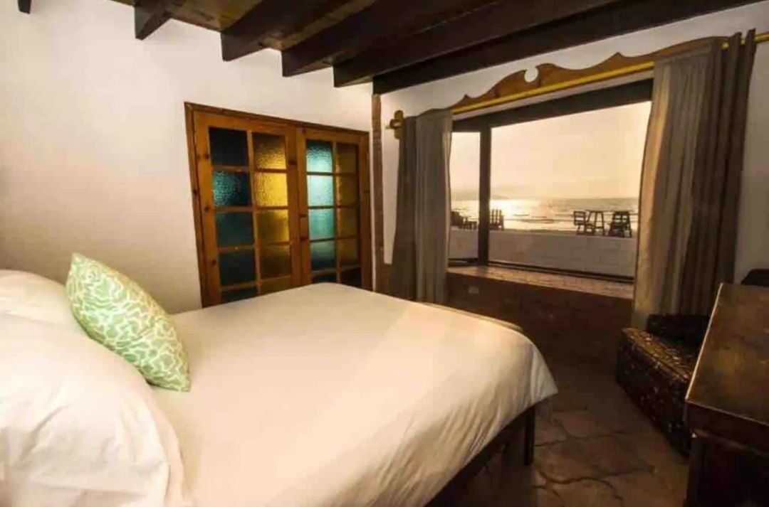 Une chambre d’hôtel avec un lit, une fenêtre donnant sur la plage et une porte en bois.