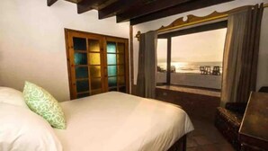 A hotel room with a bed, a window with a view of the beach, and a wooden door. - La Haciendita Beachfront Home + Private Pool (Ensenada)