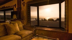 A cozy room with a sofa, a small table, and a view of the beach through large windows. - La Haciendita Beachfront Home + Private Pool (Ensenada)