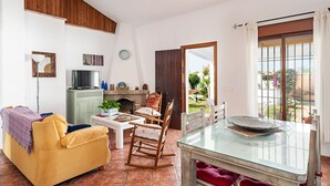 Un saló amb un sofà, cadires, una taula de vidre, una llar de foc i vista a través d'una porta.