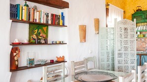 Habitació amb taula de vidre, cadires, prestatgeries, un element decoratiu a la paret i un armari verd amb vaixelles.