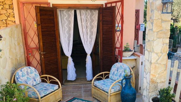 A patio with wicker chairs, a blue vase, and potted plants. - Charming Villetta Lelù with Garden and Terrace by the Sea (Villasimius)