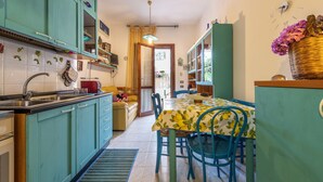 A kitchen with teal cabinets, a dining table with chairs, and a clock on the wall. - Charming Villetta Lelù with Garden and Terrace by the Sea (Villasimius)