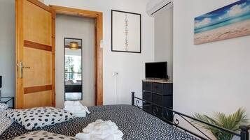 A bedroom with a bed, a wooden door, a framed artwork, an air conditioning unit, and a television.
