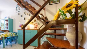 A wooden staircase with a rustic design, a dining area with blue chairs and a table, and a kitchen with teal cabinets. - Charming Villetta Lelù with Garden and Terrace by the Sea (Villasimius)