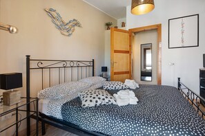 A neatly made bed with polka dot bedding, a bedside lamp, and a wall-mounted artwork. - Lelu' a Welcoming End-of-Terrace House with a Private Garden and Terrace (Villasimius)