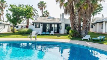 A swimming pool with lounge chairs, palm trees, and a building with a tiled roof.
