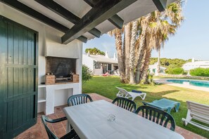 An outdoor patio with a table and chairs, a barbecue grill, and a pool in the background. - Beautiful Holiday Home in Residential Complex with Pool, Wi-Fi, Terrace and Lawn (Binisafua)