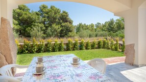 A patio with a table set for two, outdoor seating, and a view of trees and greenery. - Modern Apartment with Air Conditioning and Garden; Pets Allowed (BUDONI)