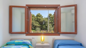 A bedroom with two beds, a window with wooden shutters, a bedside lamp, and a view of trees. - Modern Apartment with Air Conditioning and Garden; Pets Allowed (BUDONI)