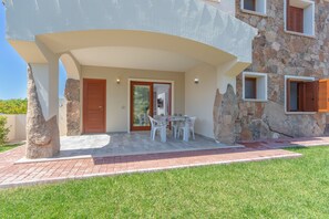 Un bâtiment moderne avec une façade en pierre, un patio couvert avec une table et des chaises, et une pelouse verdoyante.