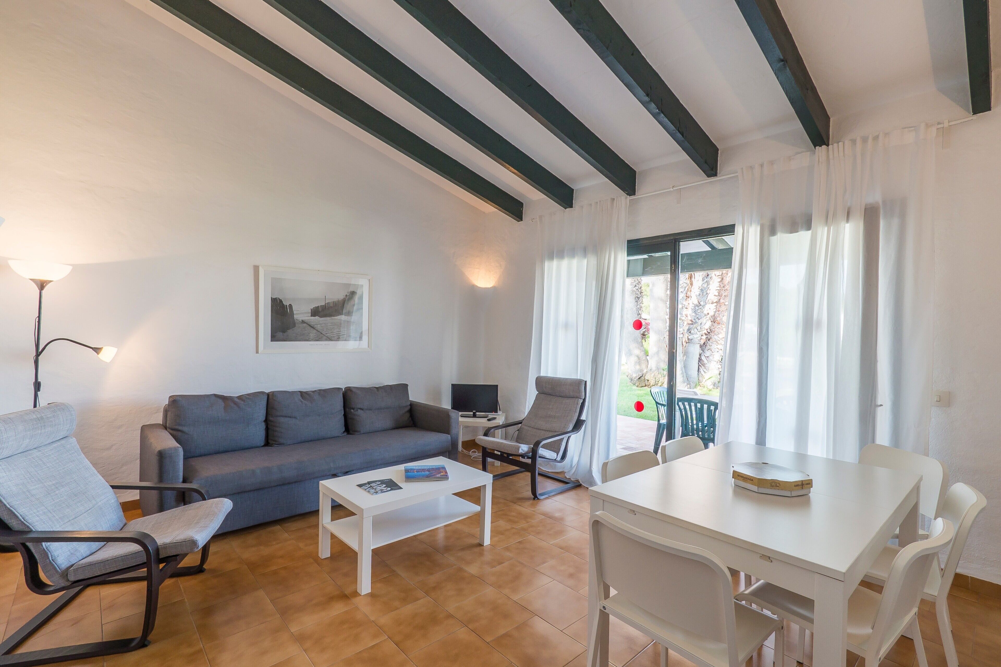 A living room with a sofa, a coffee table, a TV, and a dining table with chairs.