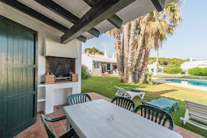 An outdoor patio with a table and chairs, a barbecue grill, and a pool in the background.
