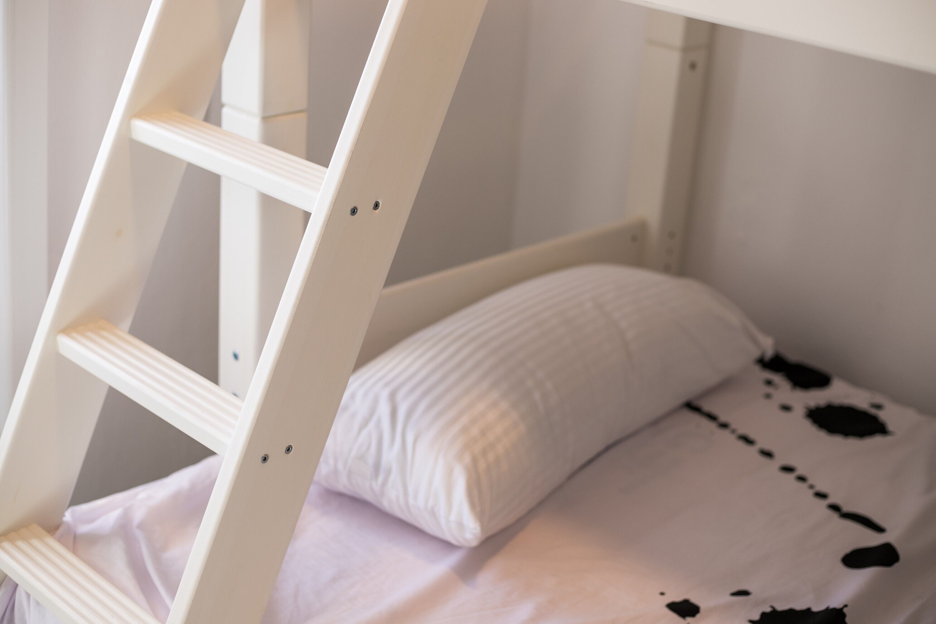 A bunk bed with a ladder, a white pillow, and a bedspread with black spots.