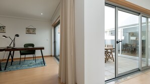 A modern interior with a desk, chair, and a view through a glass door to an outdoor dining area. - Feel Corporate Housing Marquês II (Oporto)