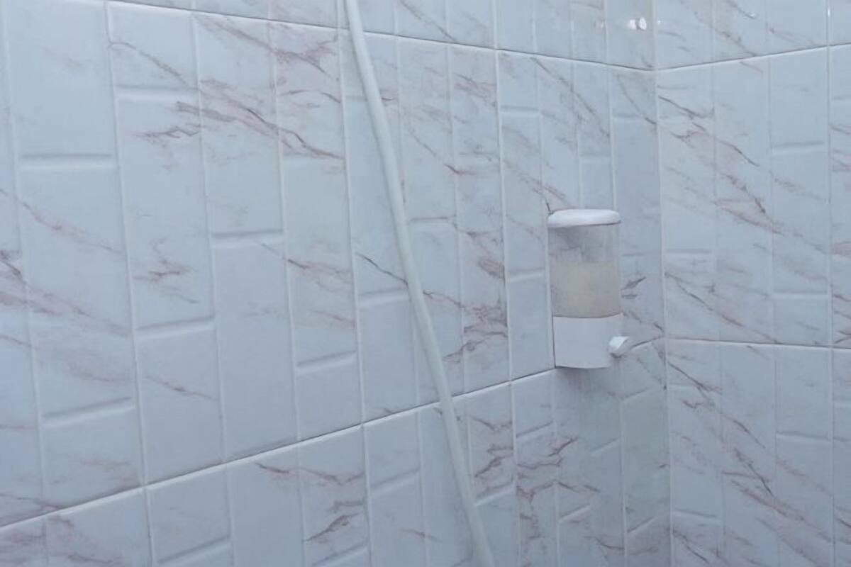 A bathroom with white marble tiles and a white soap dispenser mounted on the wall.