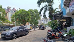 A paved street with parked cars and motorcycles, lined with trees and residential buildings. - Syariah Amethyst Cengkareng (Jakarta)