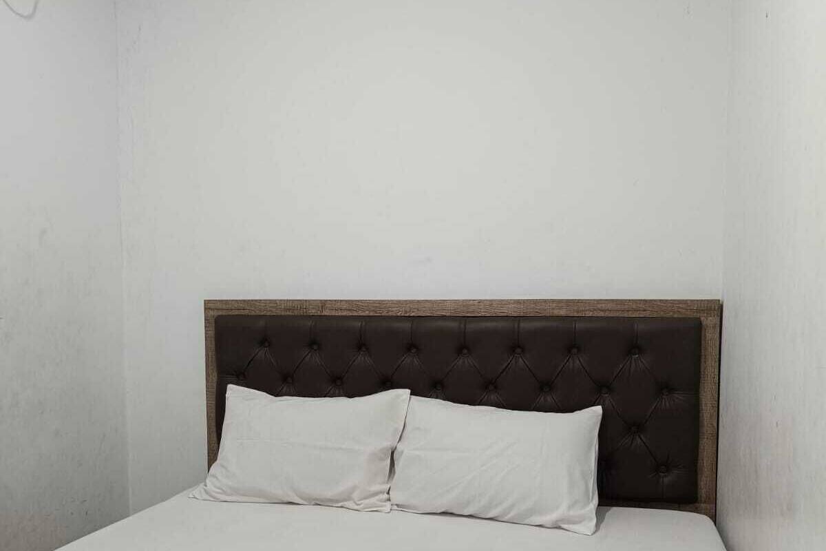 A single bed with a dark headboard and two pillows in a room with plain white walls.