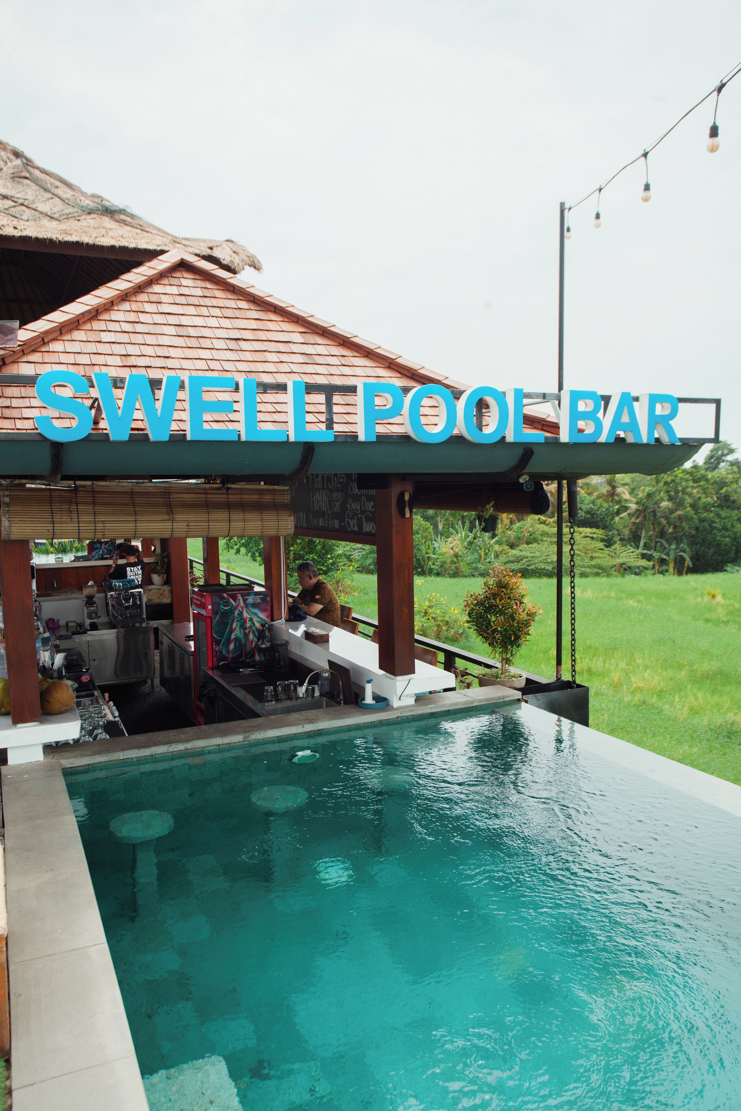 Un bar junto a la piscina con un cartel que dice "SWELL POOL BAR" y una piscina al fondo.