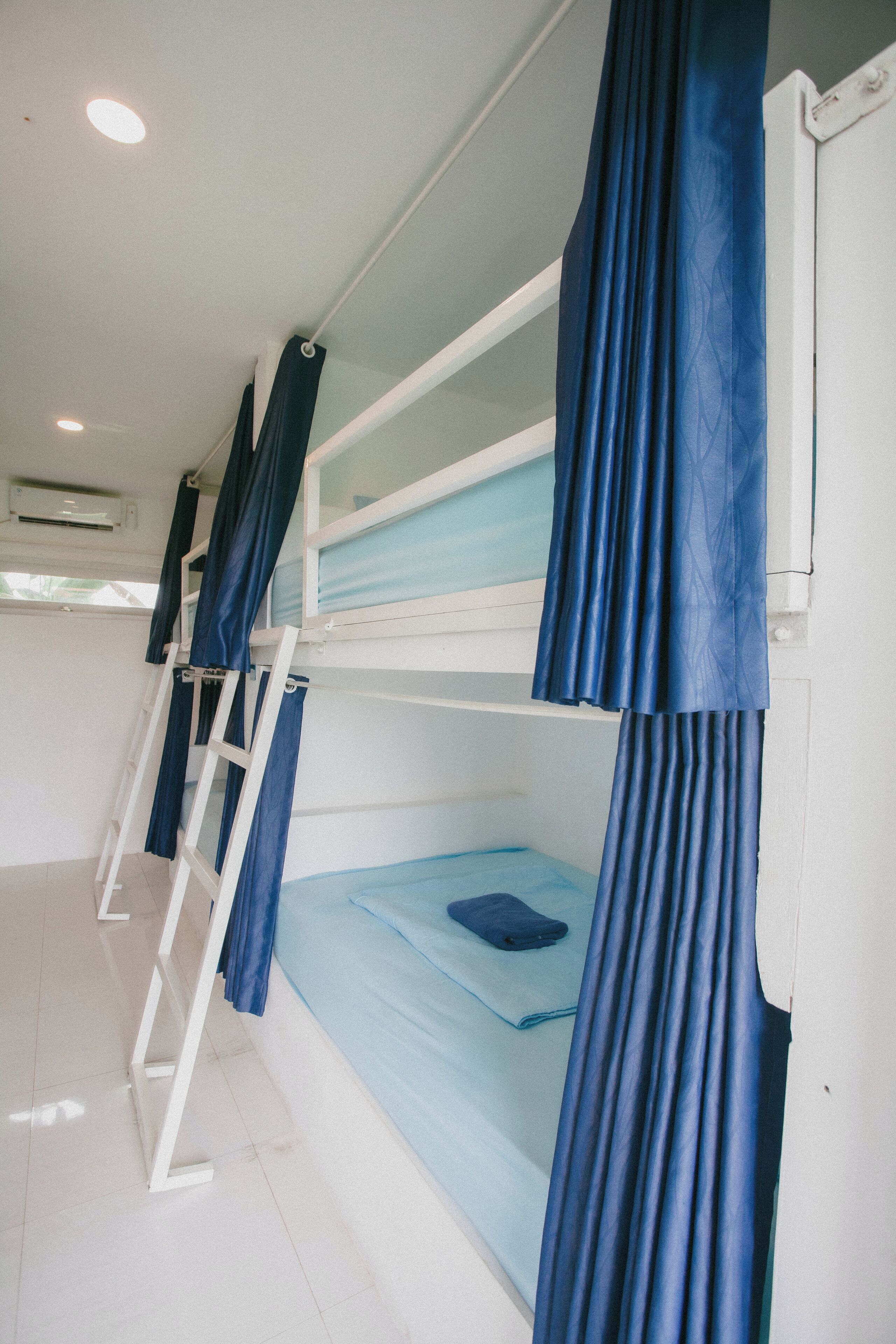 A bunk bed room with blue curtains, a ladder, and a window.