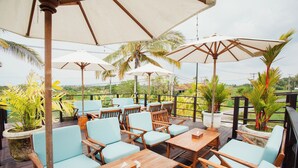 An outdoor seating area with wooden tables and chairs, surrounded by umbrellas and potted plants. - The Swell - Hostel - Adults Only (Tabanan)