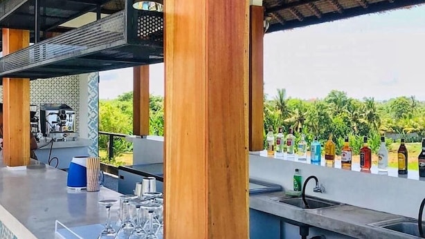 An outdoor bar area with a pool, wooden pillars, and a thatched roof. - The Swell - Hostel - Adults Only (Tabanan)