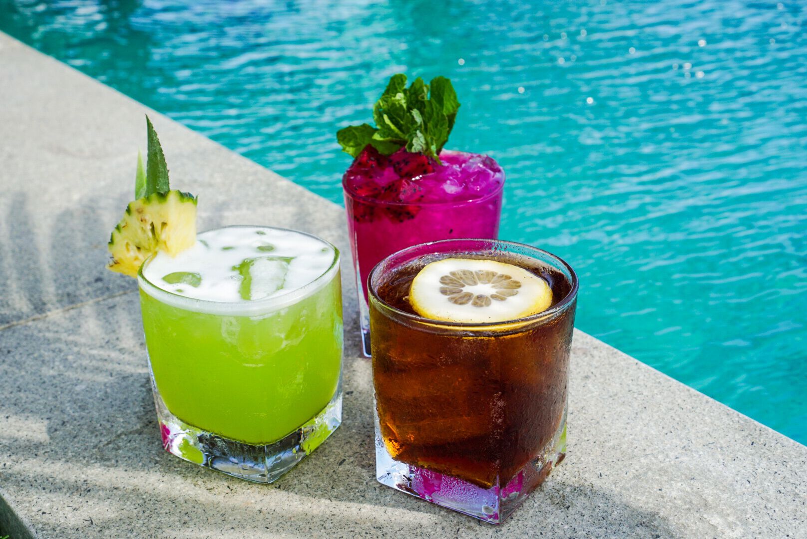 Three drinks by a poolside with a clear blue pool in the background.