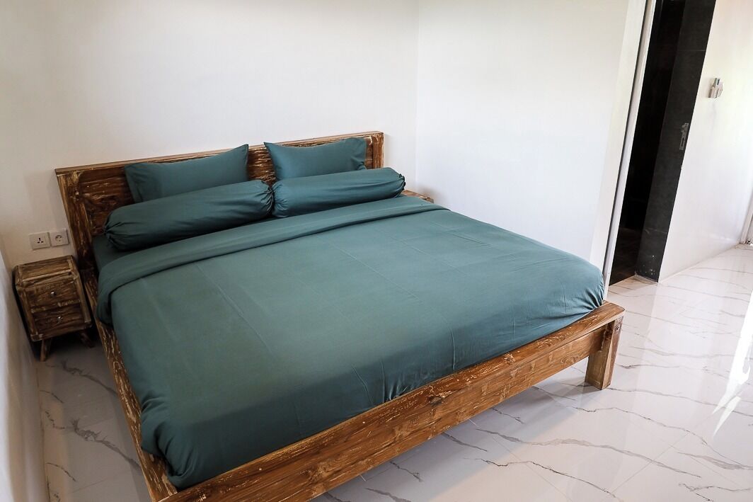 Ein Bett mit Holzbettgestell und türkisblau gestreuter Bettwäsche in einem Zimmer mit weißen Wänden und einem Marmorboden.