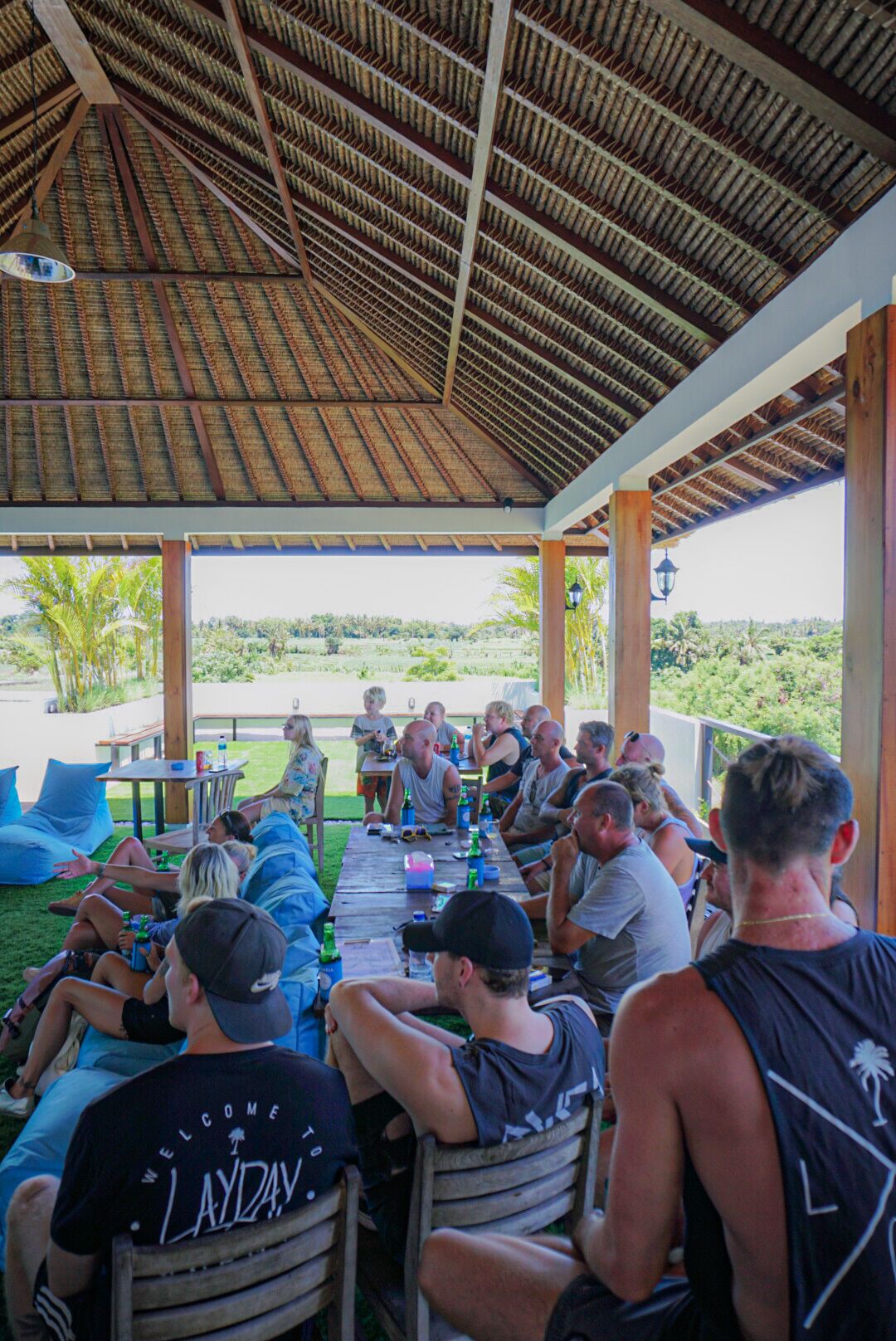 A covered outdoor seating area with a thatched roof, wooden tables, and chairs.