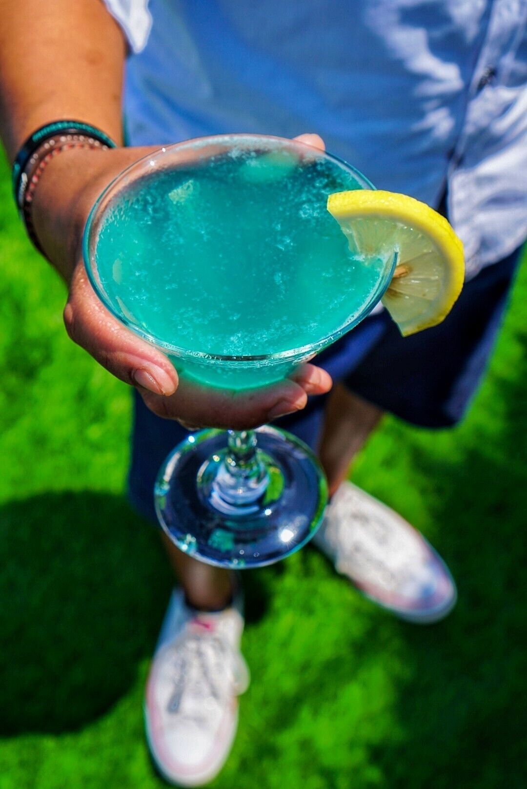 A person holding a blue cocktail with a lemon garnish.
