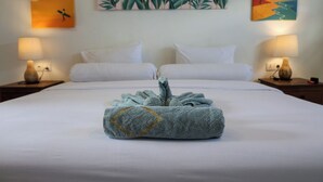 A neatly made bed with a folded towel in the center, two bedside tables with lamps, and tropical-themed wall art above the bed. - The Swell - Hostel - Adults Only (Tabanan)
