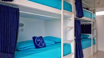 Een slaapkamer met stapelbed, slaapgedeelte in teal en gordijnen, een handdoek met de tekst 'SWELL', en een witte muur met een stopcontact.