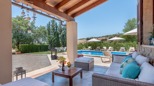 Ein überdachter Außenbereich zum Sitzen mit Pool, Korbmöbeln und Blick auf Pool und Garten.