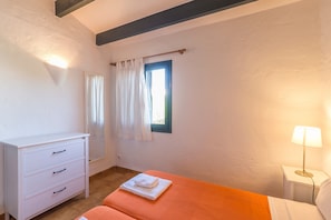 A bedroom with a bed, a bedside table with a lamp, a window with curtains, and a white dresser with drawers.