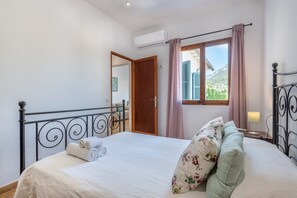 A bedroom with a bed, a window with curtains, an air conditioning unit, and a door leading to another room. - Traditional townhouse in the centre of Sóller. Air Conditioning & Wi-Fi (Sóller)