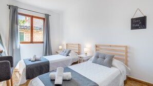 Una camera d'albergo con due letti, una finestra con tende, un comodino con una lampada e un cartello a parete.