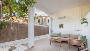 Un portico coperto con una panca in legno, un divano e un tavolo con una ciotola di frutta.