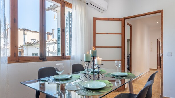 Zona pranzo con tavolo in vetro, sedie nere e vista sugli edifici attraverso una finestra.