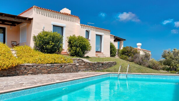 A swimming pool with a stone wall and a building with a tiled roof.