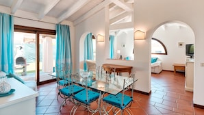 A dining area with a glass table, blue cushioned chairs, and a view through an archway to an outdoor patio.