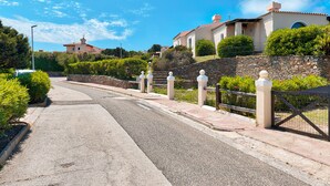 A residential street with a paved road, stone walls, and a gated entrance.