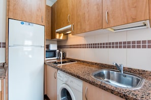 A kitchen with a stainless steel sink, a microwave, a dishwasher, and wooden cabinets.