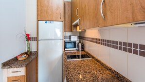 Una cocina con armarios de madera, un refrigerador, un microondas y una tetera.