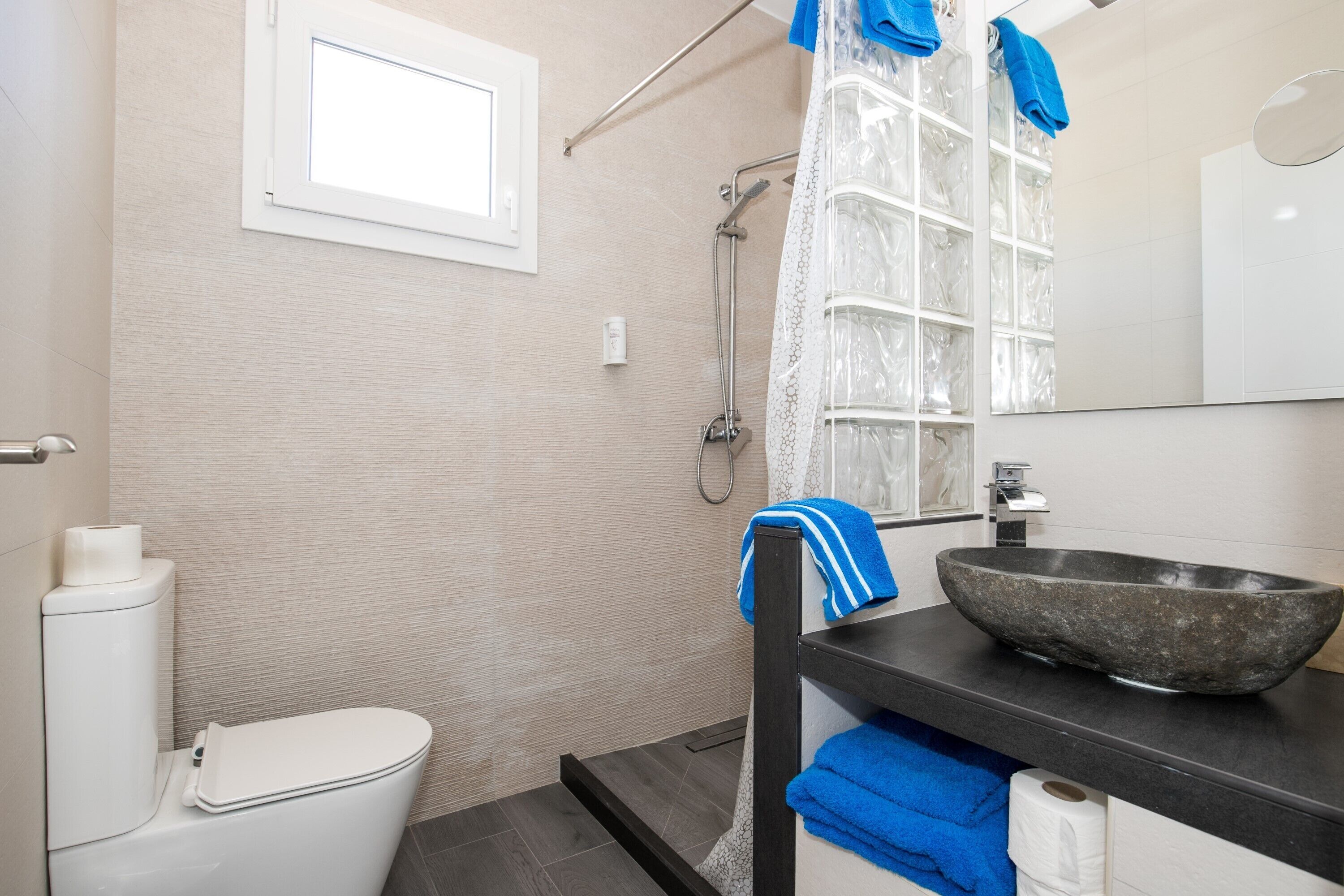 Een badkamer met toilet, douche, wastafel met stenen wasbak en spiegel.