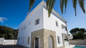 A two-story house with a stone facade, a pool, and a clear blue sky.