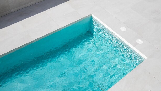 A swimming pool with clear blue water, surrounded by light-colored tiled flooring.