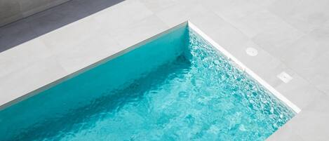 A swimming pool with clear blue water, surrounded by light-colored tiled flooring.