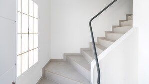 A staircase with a black handrail, a white wall, and a window with a grid pattern.