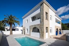 A two-story building with a swimming pool, stone arches, and a palm tree.